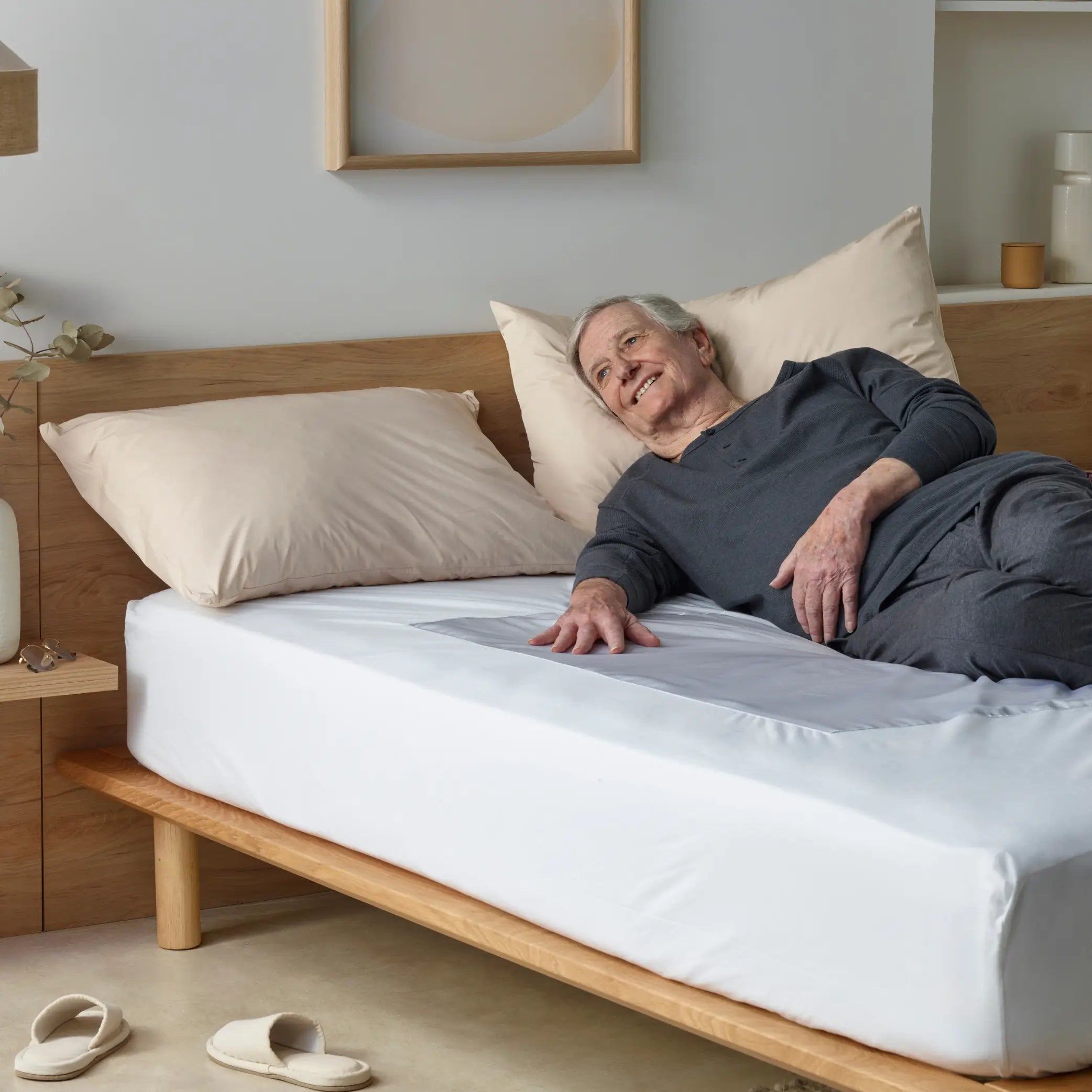 Elderly man lying on a bed with a white waterproof bed protector designed for mobility assistance. The breathable, hypoallergenic protector offers spill-proof, incontinence-friendly protection, ensuring a clean and dry sleep surface.