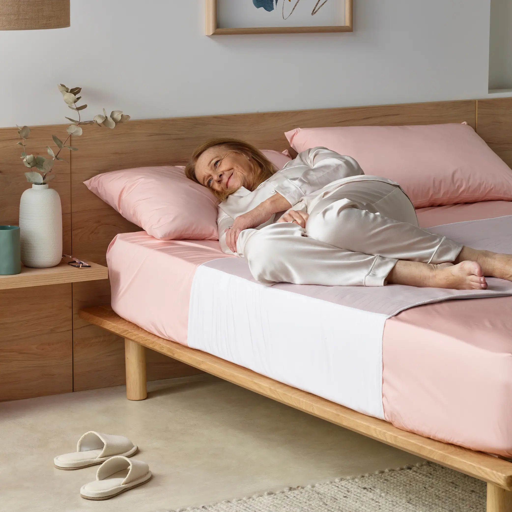 Elderly woman comfortably resting on a bed with a soft pink waterproof bed pad, known as kylie. Designed for incontinence protection, this breathable and washable bed pad keeps bedding dry and ensures a restful sleep.