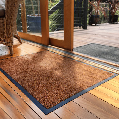 Brown doormat with blue border on a wooden floor next to a glass door.